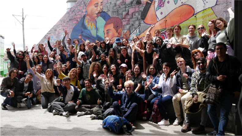 Grupo de estudiantes y profesionales reunidos frente a un mural, participando en una actividad de un programa corporativo